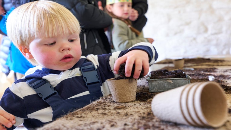 A small child filling an eco pot with soil